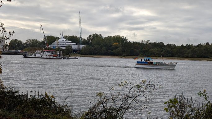 Zwei Boote fahren auf einem ruhigen Gewässer, umgeben von Bäumen und einem Gebäude im Hintergrund.