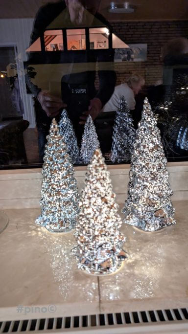 Drei dekorierte Weihnachtsbäume aus Glas stehen auf einem Tisch.