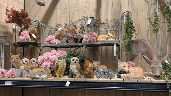 Dekorative Tierfiguren aus Holz und Keramik, umgeben von pinken Blumen.