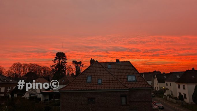 Bunte Abenddämmerung über einem Wohngebiet mit Häusern und Bäumen.