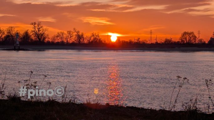 Sonnenuntergang über einem ruhigen Gewässer mit silhuettierter Uferlinie.