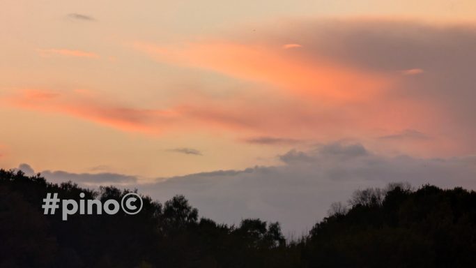 Zarte rosa Wolken über einer Landschaft bei Sonnenuntergang.