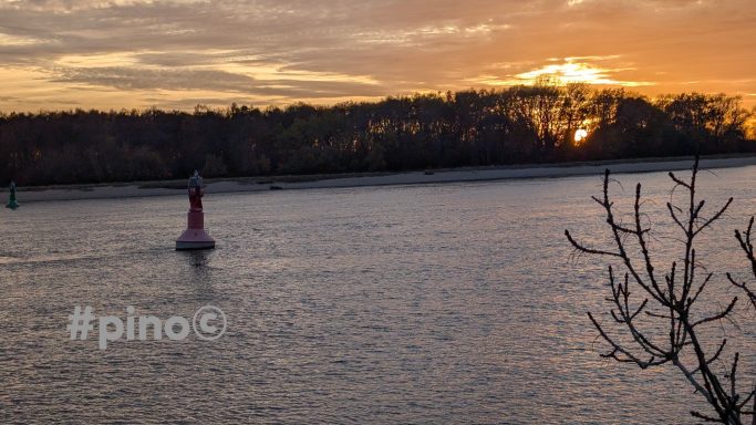 Sonnenuntergang über einem Gewässer mit Bojen und Bäumen am Ufer.