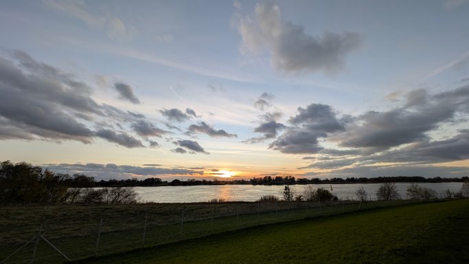 Sonnenuntergang über einem ruhigen Gewässer mit Wolken am Himmel.