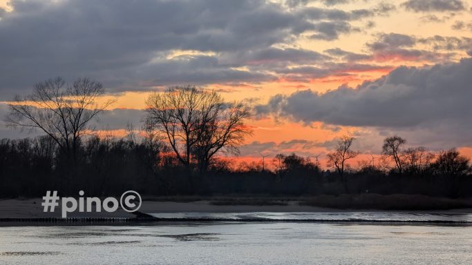 Sonnenuntergang über einem Fluss mit Wolken und Bäumen im Hintergrund.
