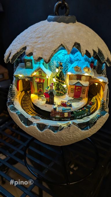 Winterlandschaft in einer beleuchteten Schneekugel mit Häusern und Tannenbaum.