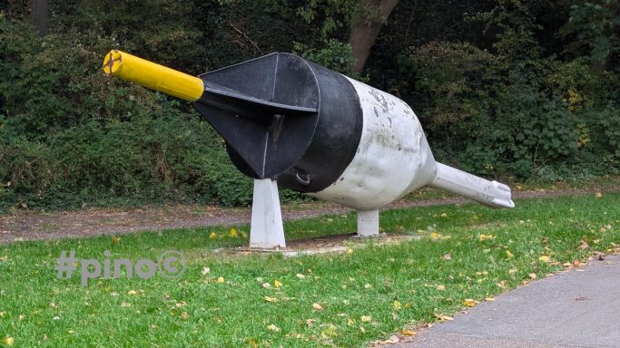Große Skulptur eines Stifts mit gelber Spitze auf einer Wiese.