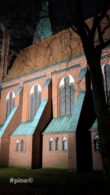 Fassade einer Backsteinkirche mit schmalen Fenstern und grünem Dach.
