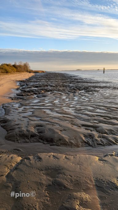 Flacher Sandstrand mit Wasser und feinen Wellen unter einem klaren Himmel.