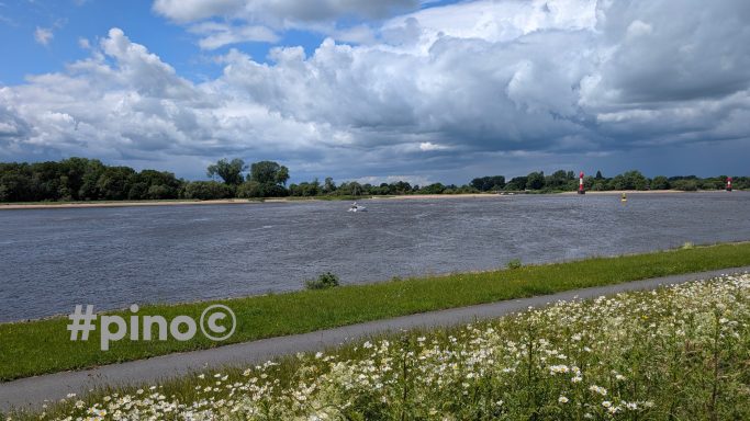 Blick auf einen Fluss mit Wiesen und Wolken am Himmel.