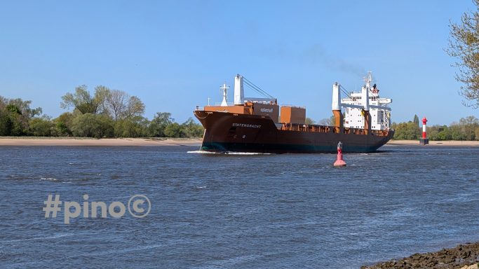 Ein Frachtschiff fährt auf einem Fluss, umgeben von Bäumen und einem roten Marker.