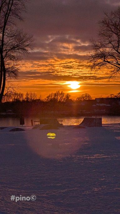 Sonnenuntergang über einem schneebedeckten See, mit reflektierenden Farben am Himmel.