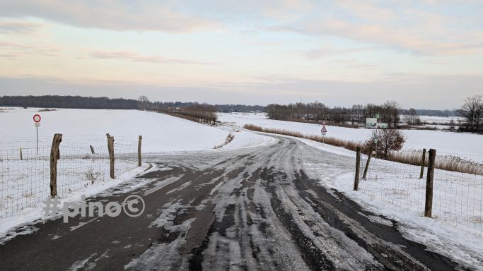 Schneebedeckte Landstraße mit Feldern und einem bewölkten Himmel.