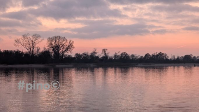 Ruhiger Fluss bei Sonnenuntergang mit reflektierendem Wasser und Bäumen im Hintergrund.
