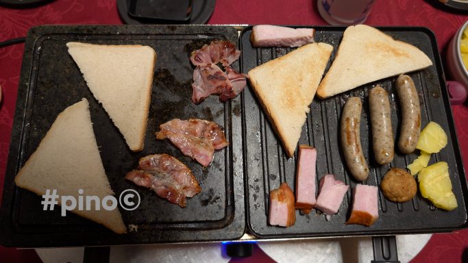 Gegrillte Toastscheiben, verschiedene Fleischsorten und Wurst auf einer Grillplatte.