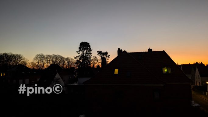 Dämmerung über einem Wohngebiet mit beleuchteten Fenstern und silhouettierten Bäumen.