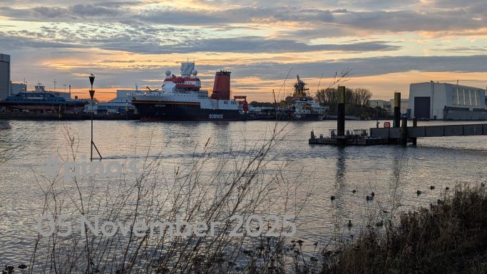 Wasserspiegel mit Booten und einem Hafen im Hintergrund bei Sonnenuntergang.