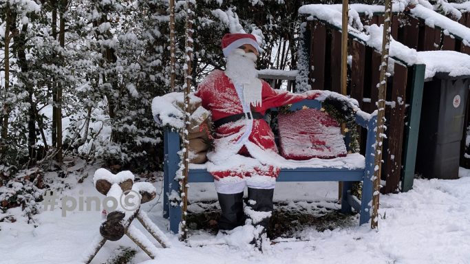 Ein Weihnachtsmann in einem roten Anzug sitzt auf einer Bank, umgeben von Schnee.