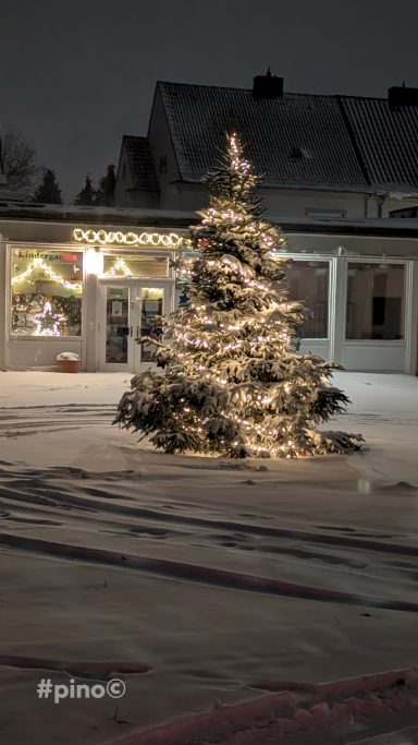 Ein beleuchteter Weihnachtsbaum im Schnee bei Nacht.