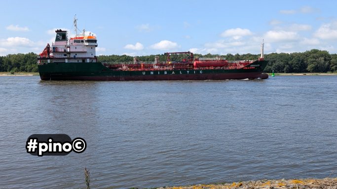 Ein großes Frachtschiff fährt auf einem ruhigen Fluss unter blauem Himmel.