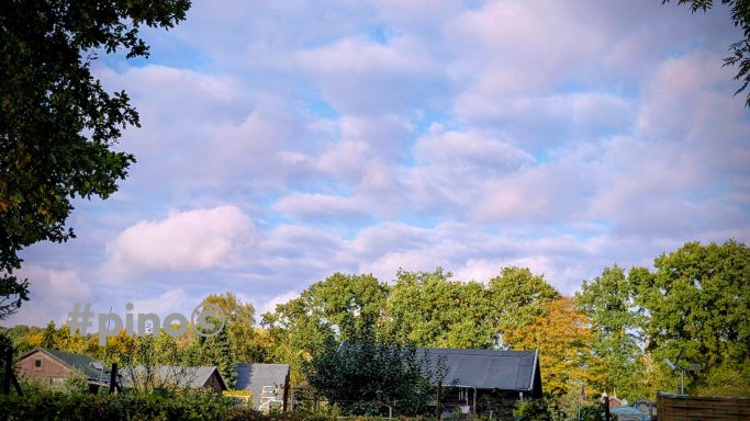 Blaue Himmel mit Wolken über ländlicher Landschaft mit Häusern und Bäumen.