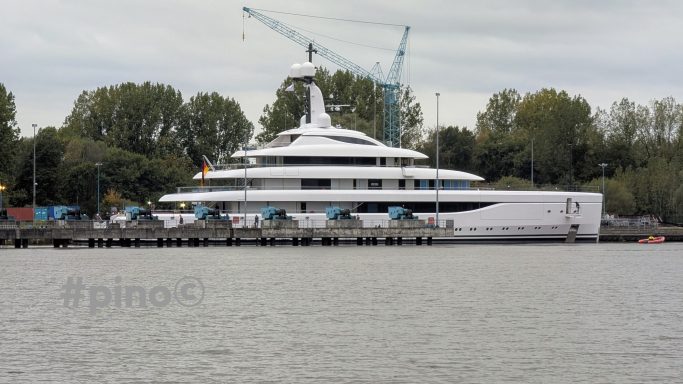 Luxusyacht am Hafen, umgeben von Bäumen und Baukränen im Hintergrund.