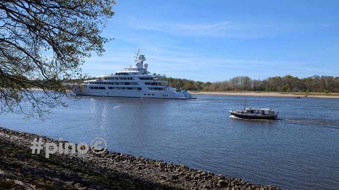 Luxuriöses Yacht auf einem ruhigen Fluss, mit einem kleineren Boot im Vordergrund.