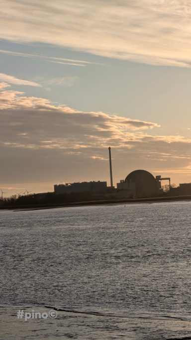 Blick auf ein Industriegebäude mit Schornstein am Wasser bei Sonnenuntergang.