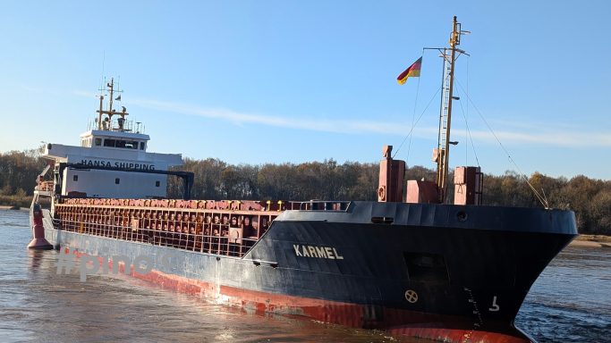 Ein Frachter mit deutscher Flagge fährt auf einem ruhigen Fluss.