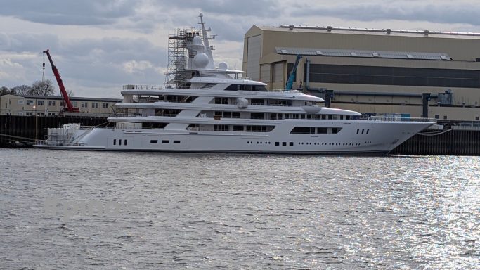 Weiße Yacht am Hafen mit einem großen Gebäude im Hintergrund und grauem Himmel.