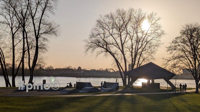 Sonnenuntergang über einem See mit Bäumen und einer überdachten Terrasse.