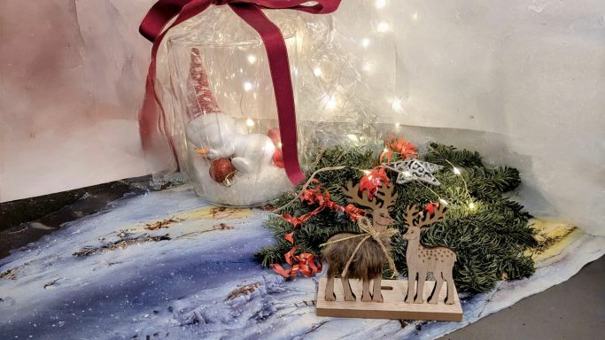 Weihnachtliche Dekoration mit einer Glasglocke, einer Holzanimalfigur und Tannenzweigen.