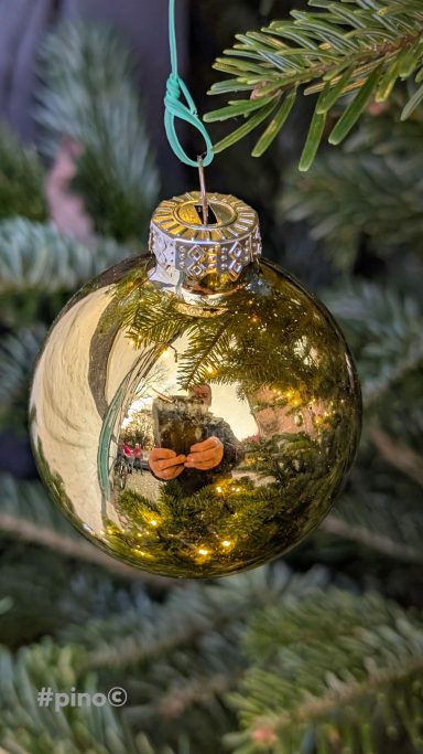 Goldene Weihnachtsbaumkugel hängt an einem grünen Tannenbaum.