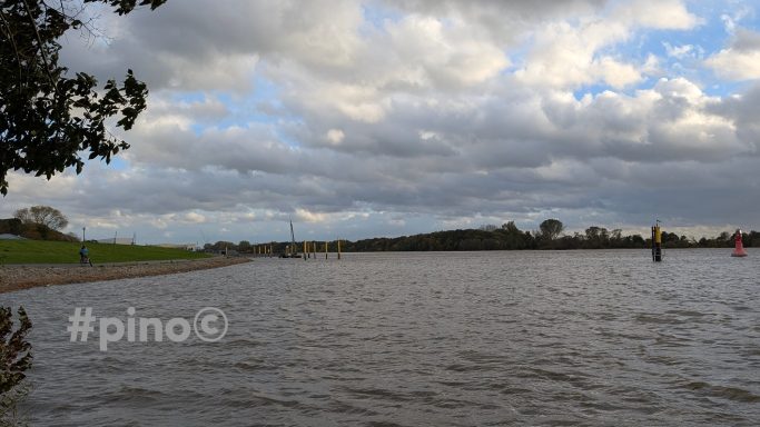 Ruhiges Gewässer unter einem bewölkten Himmel mit grünen Uferbereichen.