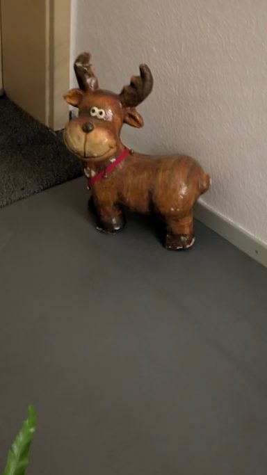 Ein brauner, dekorativer Rentier mit Geweih steht an einer Wand.