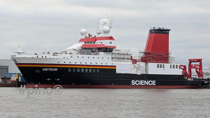 Rotes Forschungsschiff mit dem Schriftzug "SCIENCE" am Hafen.