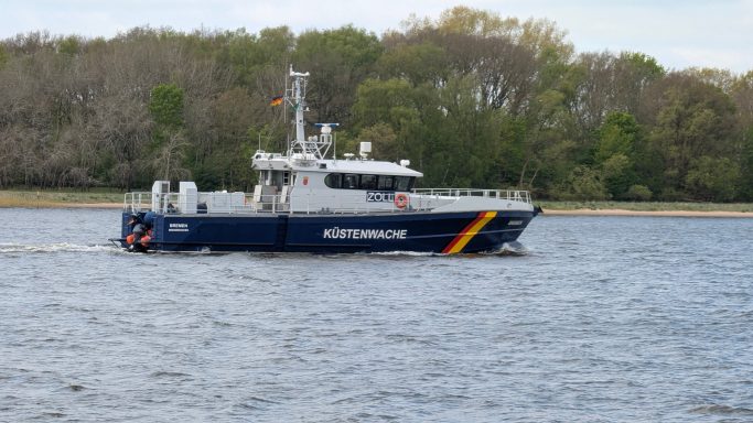 Ein blaues Patrouillenboot auf einem Gewässer, umgeben von Bäumen im Hintergrund.