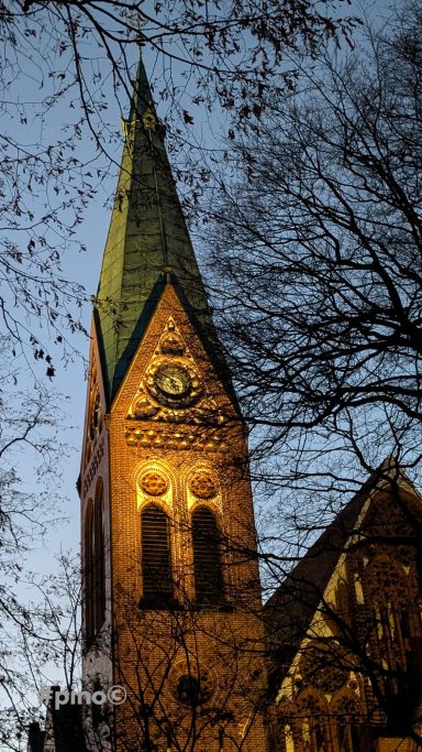 Dunkler Himmel hinter einer beleuchteten Kirchturmspitze mit grüner Dachspitze.