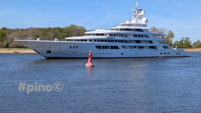 Luxusyacht fährt auf ruhigem Wasser, umgeben von Bäumen und einem roten Marker.