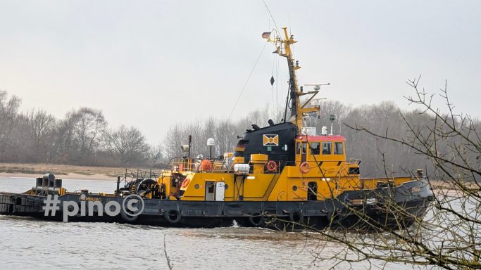 Gelber Schlepper auf einem ruhigen Fluss, umgeben von Bäumen im Hintergrund.