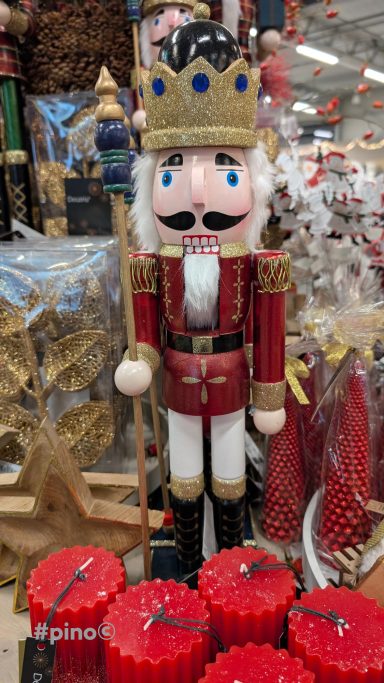 Ein dekorativer Nussknacker in rotem Anzug mit Krone und Zepter, umgeben von Weihnachtsdeko.