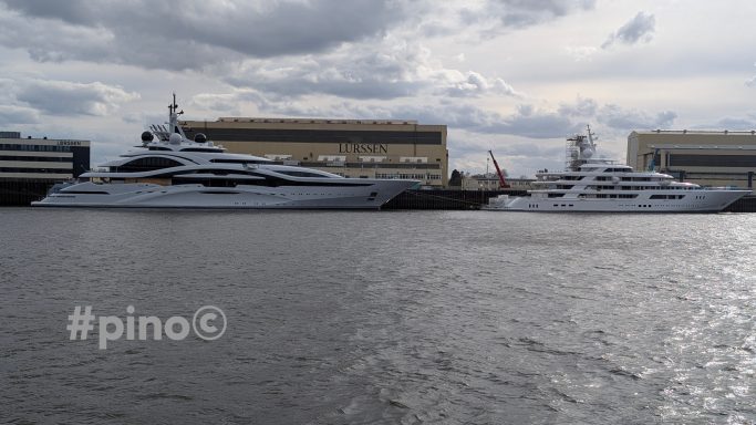 Zwei Yachten liegen im Hafen, umgeben von Wolken und einem Industriegebäude im Hintergrund.