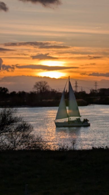 Segelboot auf ruhigem Wasser bei Sonnenuntergang, umgeben von bewölktem Himmel.