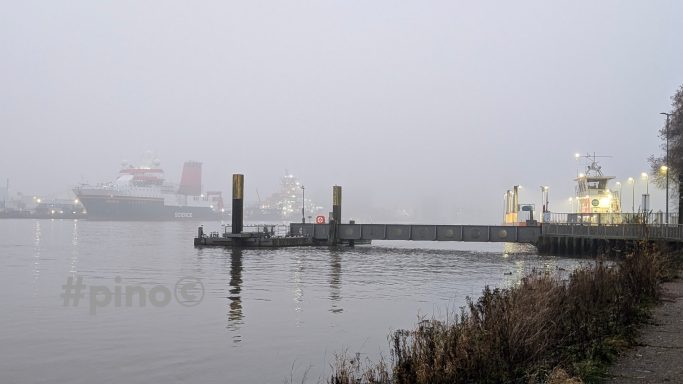 Nebelige Hafenansicht mit Schiff und Pier am ruhigen Wasser.