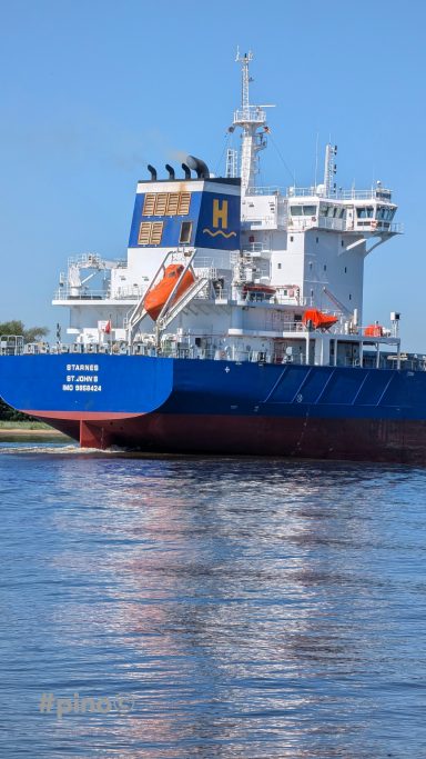 Rotes Frachtschiff mit orangefarbenen Rettungsbooten auf ruhigem Wasser.