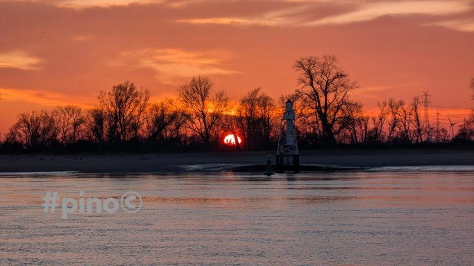 Sonnenuntergang über dem Wasser mit silhouettierten Bäumen und einem Reiter.