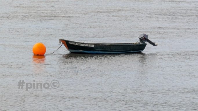 Ein kleines Boot schwimmt auf ruhigem Wasser neben einer orangefarbenen Boje.