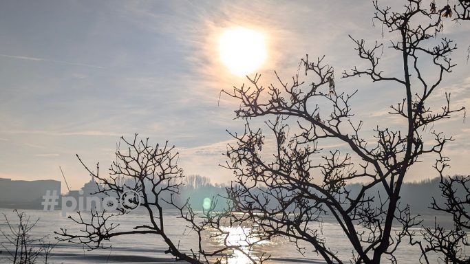 Sonnenaufgang über Wasser mit silhouettierten Ästen im Vordergrund.