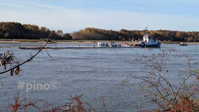 Ein Boot transportiert Fracht auf einem ruhigen Fluss mit umgebenden Bäumen.