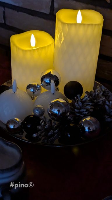 Zwei leuchtende Kerzen auf einem Tablett mit silbernen und schwarzen Dekorationen.